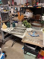 Overview of farmhouse decor items arranged on table including wooden signs, candles, faux plants, baskets, metal bins, and rooster figure.