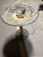 Full view of metal birdbath showing round basin with chipping paint and decorative base.