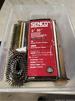 Top down view of plastic bin containing various Senco finish nails collated for pneumatic nail guns and boxes with branding visible
