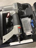 Front view of Porter Cable pneumatic nailer in black carrying case with small clear plastic container for nails.