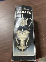 Photo of the original retail box showing the silver plated carafe with its stand depicted on the box.