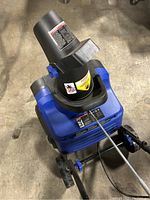 Top view of blue and black electric snow machine showing snow discharge chute and brand labels.