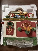 Top-down view showing ceramic stove diffuser in styrofoam box, detailing front panel with green knobs and red doors, decorated with teddy bears and holiday foliage.
