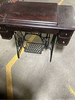 Overall view of the vintage Singer sewing machine built into a dark wood table with cast iron base and drawers.