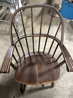 Front view of vintage wooden desk chair showing rounded backrest, vertical spindles, armrests, and seat with a scratch.