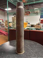 Full vertical view of the shell casing standing upright on a surface, showing cylindrical body and patina.