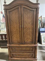 Full front view of the wood armoire showing double doors, two lower drawers, and carved woven basket-like design on the pillars and top molding.