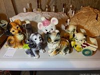 Six ceramic animal figurines displayed on a table, including dogs, a cat, and a bear with a pink party hat.