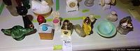 Overview of Avon collectible perfume bottles and decorative soap bowl arranged on a white surface. Various shapes include cat, lantern, chair, birdhouse and more.