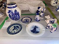 Overview photo of eight blue and white ceramic items including Royal Cauldon jar, Delft mini plates, bell, salt and pepper shakers, and figurine.