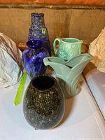 Photo showing all five ceramic items including four vases and one pitcher on a white surface with a basement background.