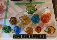 Top down view of all 10 colored glass vessels arranged near measuring ruler showing sizes around 3 to 5 inches tall, various colors and shapes.