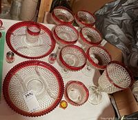Set of diamond cut glassware pieces with prominent red rims, including footed bowls, flat dishes, salt and pepper shakers, and a tumbler arranged on a table.