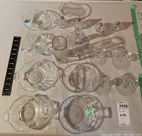 Overhead view of 17 vintage clear glass pieces including bowls, candle holders, vase, salt and pepper shakers, and a small drinking glass, arranged on a table with measurement scale.