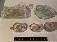 Overview of glassware lot showing trays, cream and sugar bowls, drinking glasses with ball handles, and a covered jar with gold accent lid.