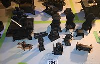 Lot arranged with miniature cast iron stove, wing back chairs with ottoman, miniature train, Liberty Bell, grandfather clock, and ship wheel on stand, shown on tabletop with yellow tape lines.