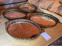 Four oval metal-framed mirrored trays placed on a surface, showing their ornate edges and mirrored bases.