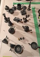 Full view of all pewter miniatures laid out on cloth, showing assortment including irons, pots, candlesticks, cannon, watering can, mugs, and small items.