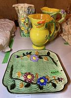 Group photo showing three ceramic pitchers and one decorative plate with floral and butterfly designs