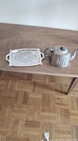 Photo showing the silverplate coffee pot and matching rectangular tray with decorative handles placed on a wooden table.