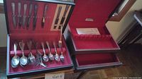 Photo of silverplate flatware including various forks, spoons, and spreaders arranged in a red-lined storage case with knives visible on the lid.