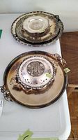Top view of three silverplate trays stacked showing pierced and decorative handles, tarnished surfaces and flower frog bud bowl on top.