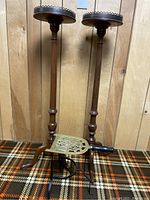Photo showing two wooden decorative pillar stands with metal trim and the fireplace spider in front, placed on a patterned carpet background and wooden wall.