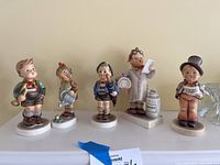Five Hummel figurines shown side by side on a white shelf.