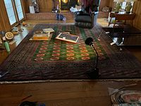 Full view of rug in living area showing green field with red medallions and intricate border.