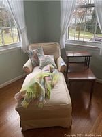 Chaise lounge with pillows, wool throw, and vintage telephone table positioned near windows in a room.