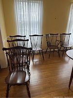 Six wooden dining chairs arrayed in room with two armchairs at front and four side chairs at rear