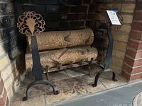 Pair of heavy iron andirons inside a brick fireplace with logs behind them.