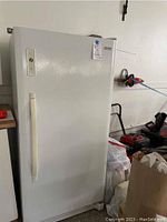 Front view of the white Kenmore upright freezer in a garage area with handle on the left side and closed door.