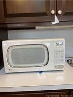 White LG microwave with retro curved glass front and control panel on the right side, placed on kitchen counter.