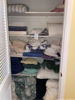 Closet shelving filled with assorted folded bed linens, pillows, and blankets visible on multiple shelves.