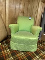 Front view of lime green mid-century armchair against wood panel wall and plaid carpet, showing fabric pattern and overall shape.