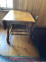 Side view of the wooden drop leaf table showing turned legs and drop leaf mechanism.