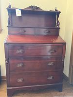Front image of petite secretary desk closed showing carved wood pulls and wood finish.