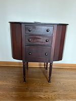 Front view of vintage sewing table showing three drawers and closed side compartments.