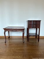 Wood carved coffee table with glass topper next to wooden nightstand with drawers and shelf.