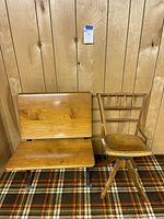 Front view of two vintage wooden chairs: a large folding chair with solid wood seat and back and a smaller swivel chair with an upholstered seat and spindle backrest.
