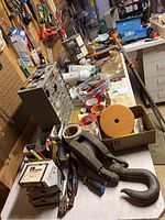 Full view of workbench surface loaded with hardware, fasteners, tapes, small metal hooks, large metal clamp hooks, and a Bernz-o-matic torch.