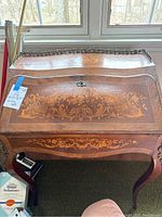 Front view of vintage wooden writing desk with floral inlay and metal gallery rail on top edge.