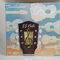 Front cover of the J.J. Cale Troubadour album showing a guitar headstock with a treble clef and cloudy sky background.