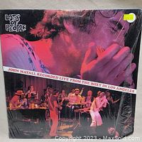 Front cover of John Mayall's 'Lots of People' live album vinyl record showing John Mayall playing harmonica, with band performing on stage.