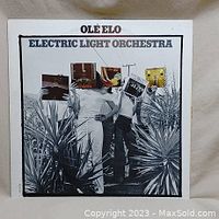 Front cover of 'Olé ELO' album by Electric Light Orchestra showing artistic black and white photo of three men with album covers on their heads.