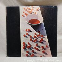Front cover of the vinyl record album showing a black cover with a central photo of a white bowl with red liquid and scattered red pellets casting shadows.