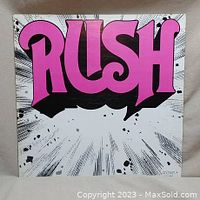 Front cover of the Rush self-titled debut vinyl album with large pink and black logo text on a white burst background.