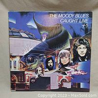Front cover of The Moody Blues - Caught Live + 5 album showing colorful surreal artwork with band member portraits and text.