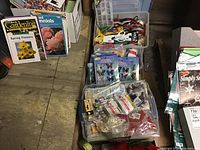 Bins filled with craft supplies placed on a wooden floor showing scissors, adhesive materials, and decorative stickers.